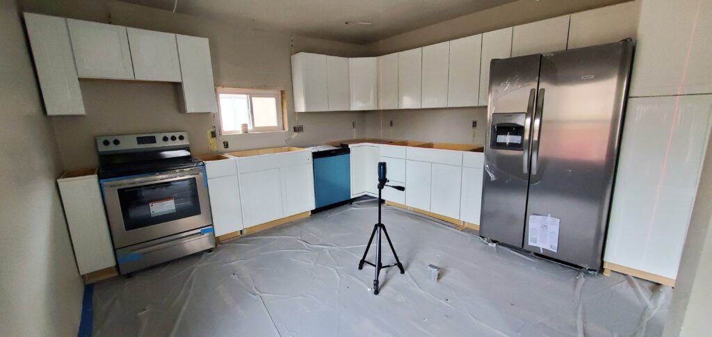 Kitchen installation in progress showing white cabinetry and stainless steel appliances setup