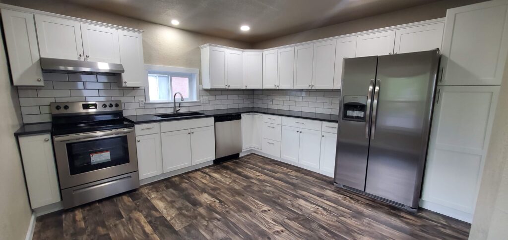 Modern kitchen remodel with white cabinetry, black countertops, subway tile backsplash, and stainless steel appliances